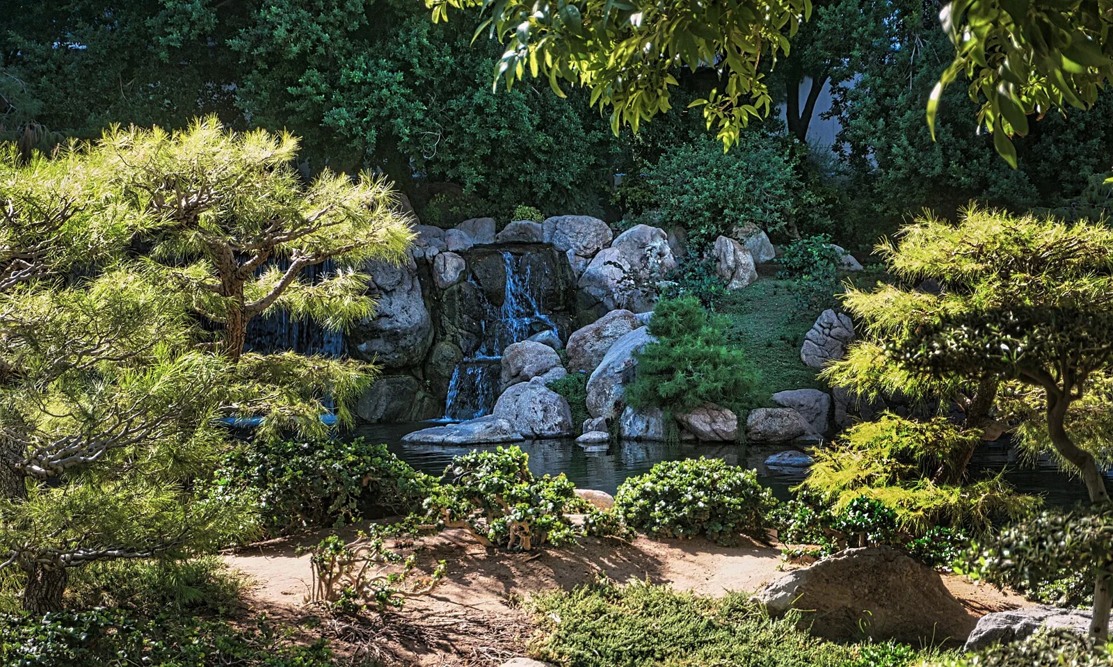 A rocky waterfall pouring into a pond, framed by clipped pines and green shrubs at the Japanese Friendship Garden
