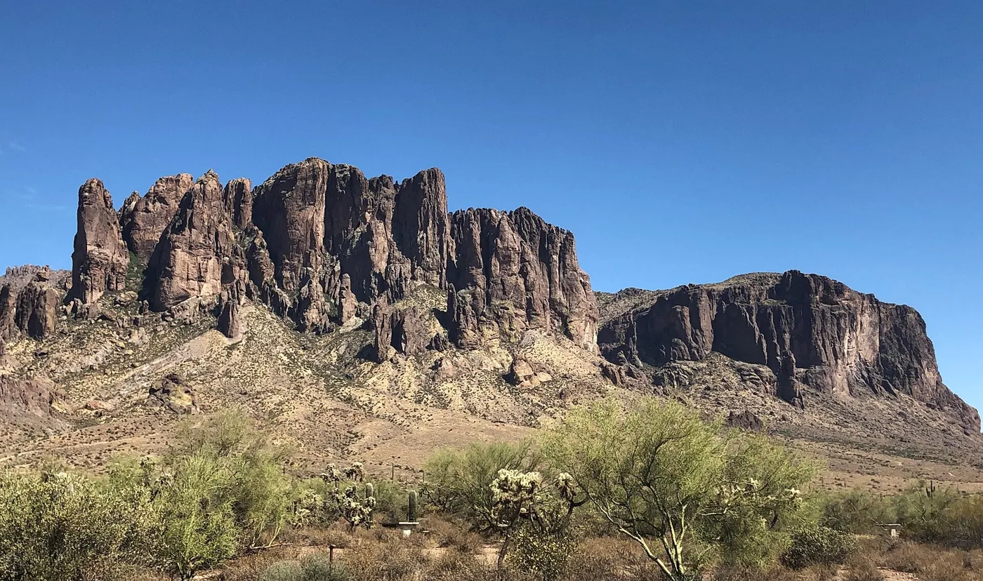 The jagged rock face of the Superstition Mountains above green desert scrub under a clear blue sky